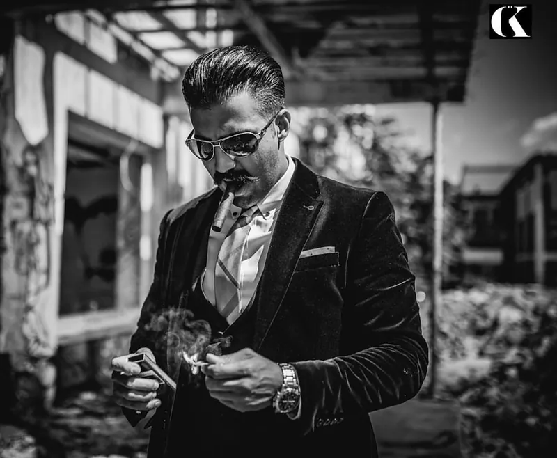 Ömer Kaya im Samtsakko mit Sonnenbrille zündet sich etwas an, schwarzweiß