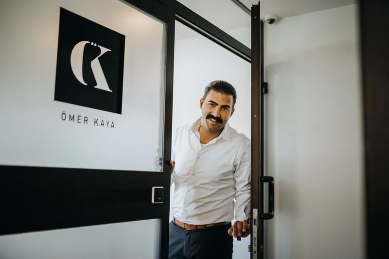 Ömer Kaya öffnet eine Glastür, daneben sein Logo ÖK
