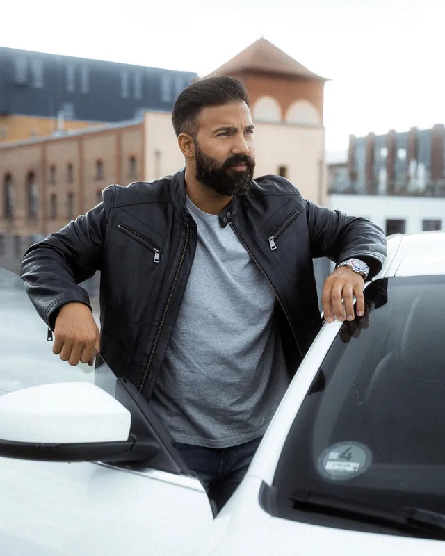 Ömer Kaya in Lederjacke lehnt an der offenen Tür eines weißen Wagens