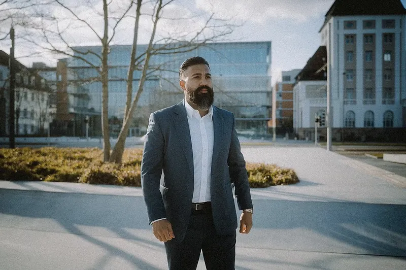 Ömer Kaya im blauen Anzug auf einem Platz vor Bürogebäuden