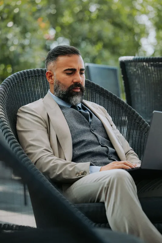 Ömer Kaya im beigen Anzug mit Laptop in einem Korbsessel