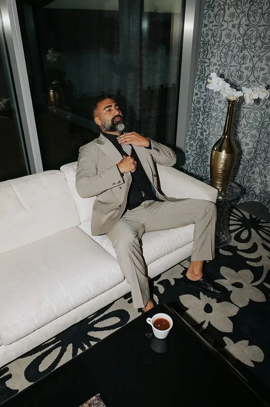 Ömer Kaya im beigen Anzug auf einem weißen Sofa neben einer goldenen Vase in Dubai
