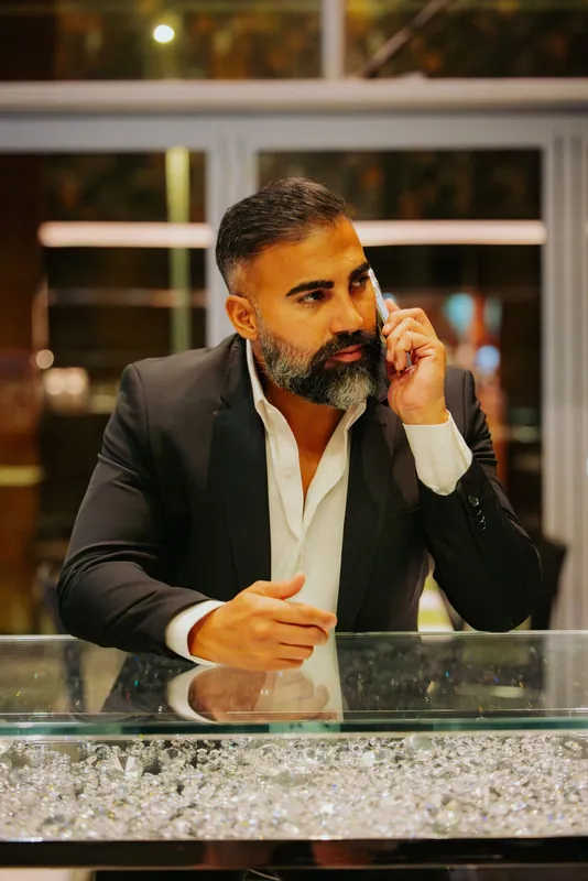Ömer Kaya im schwarzen Anzug, das Telefon am Ohr, an einer Glasvitrine