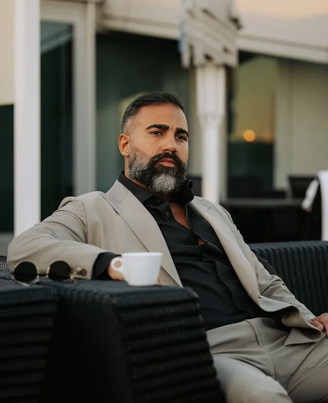 Ömer Kaya im beigen Anzug mit Kaffeetasse auf einer Terrasse